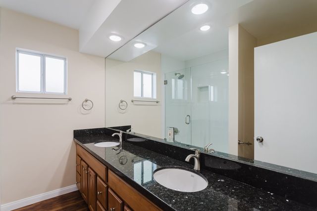 Bathroom with a dual-sink vanity, dark stone counter, wide mirror and a glass-enclosed shower