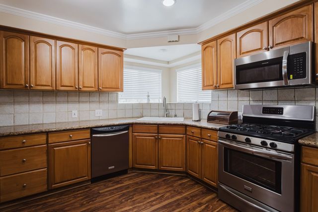 Kitchen with wood cabinets, tile backsplash, stainless steel gas range, microwave and dishwasher