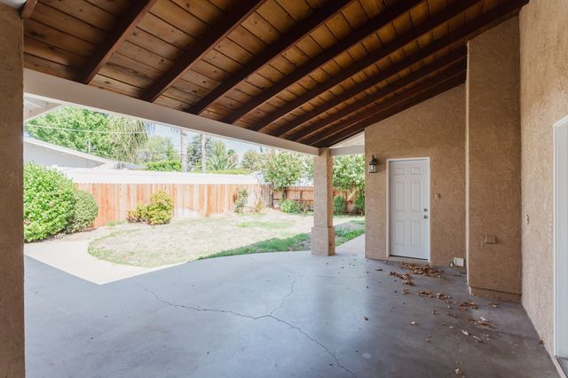 Covered patio with an exposed wood beam ceiling opening to a fenced backyard