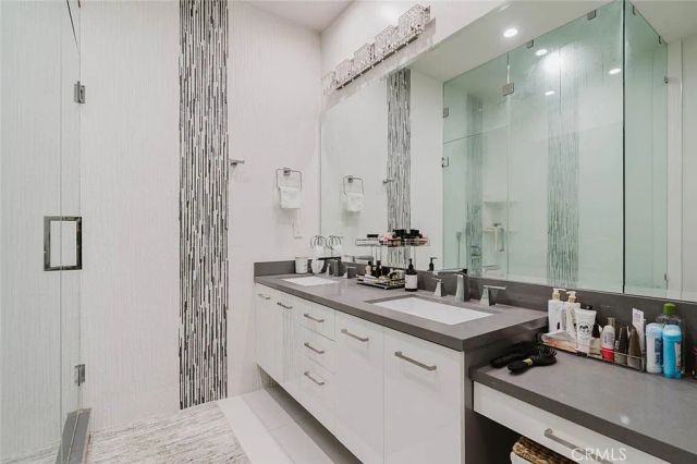 Updated bathroom with double vanity, wide mirror and glass-enclosed shower