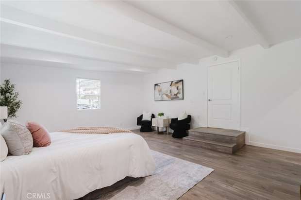 Primary bedroom with an exposed wood beam ceiling, wood flooring and a small sitting area