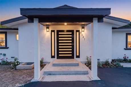 Front exterior of 8547 Louise Avenue at dusk with a modern wood entry door, covered porch and landscaped walkway
